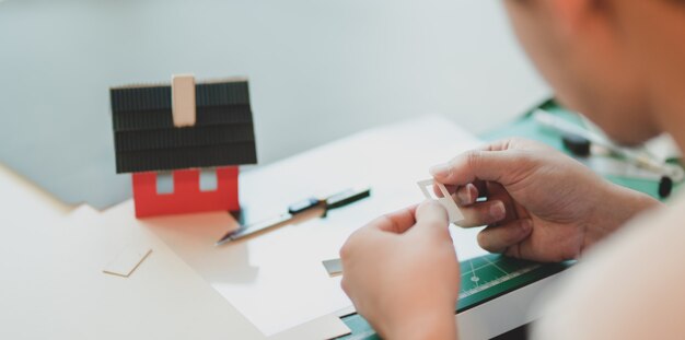 Close-up view of young male architect making small house model 