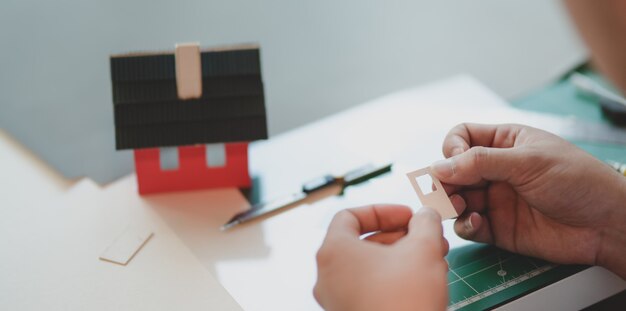 Close-up view of young male architect making small house model 