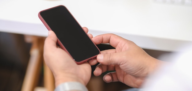 Close-up view of young man holding smartphone in modern office room