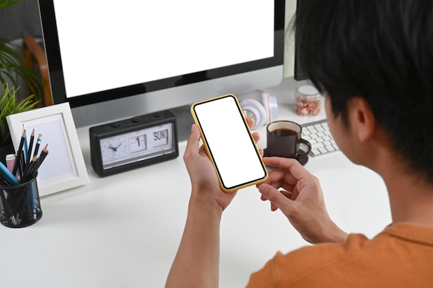 Close up view of young man sitting at his workspace and using mobile phone