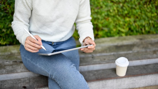 Close up view of young woman using tablet while sitting in the park with coffee cup