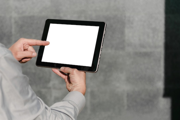 Foto close-up, vinger voor een tabletschermmodel, in de handen van een zakenman. tegen de achtergrond van een grijze betonnen muur.