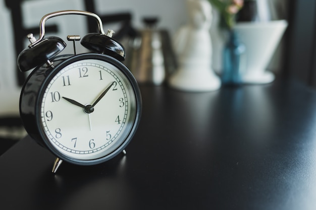 Photo close up vintage black alarm clock placed on a black wooden table, blurred background