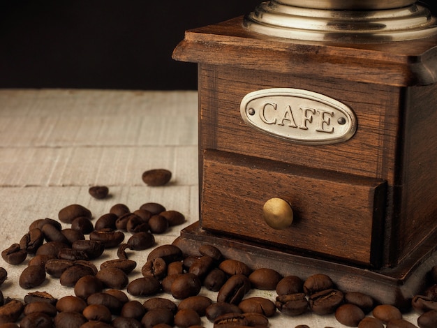 Close-up vintage coffee grinder mill with coffee grains on a dark and light wooden background.