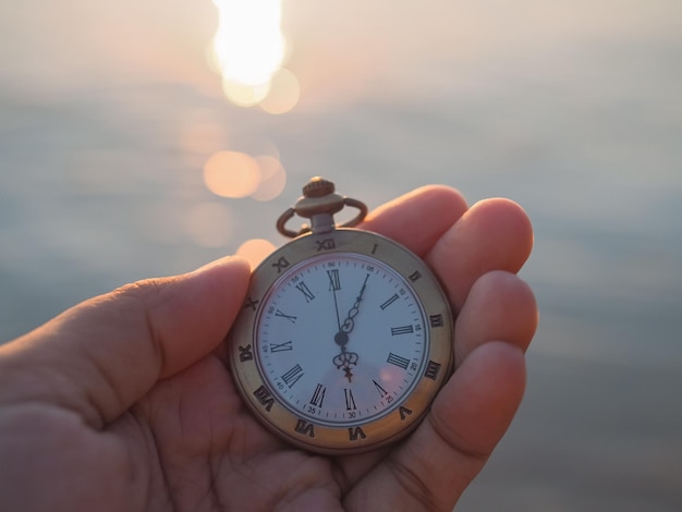 Close up of vintage pocket watch in woman hand with sea in the sunset time as background