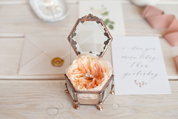 Close-up vintage wedding jewelry box for wedding rings on a wooden table with a greeting card and flowers.