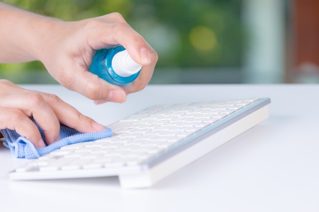 Close-up vrouw handen met behulp van alcohol spray om toetsenbord te reinigen tegen de ziekte van Coronavirus (Covid-19)