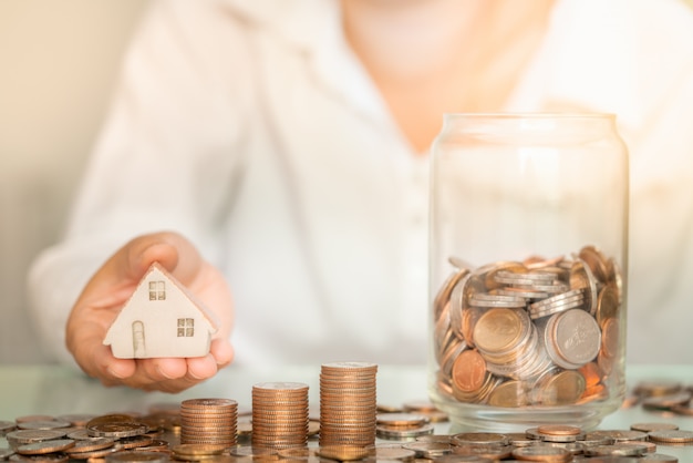 Foto close-up vrouw met huis figuur met munten stapel en glazen pot op tafel. bedrijfs- en spaargeld concept.