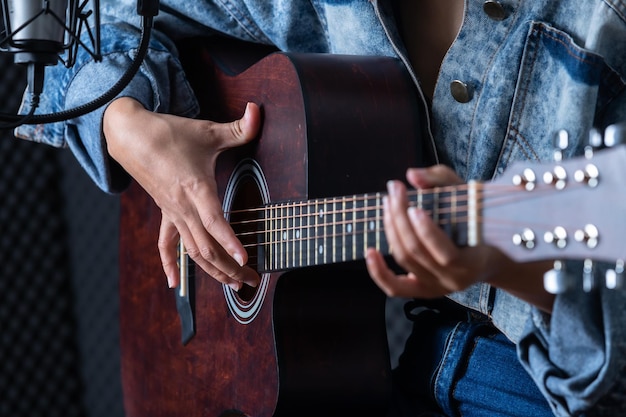 Close-up vrouw vingers met bemiddelaar met een gitaar die een lied opneemt in de opnamestudio