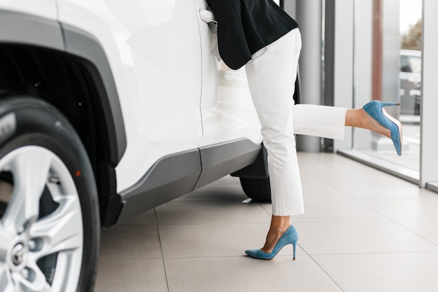 Close-up vrouwelijke benen - vrouw die op witte auto wordt geleund.