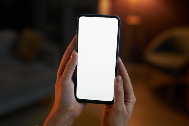 Close-up vrouwelijke hand met telefoon met wit scherm mockup thuis