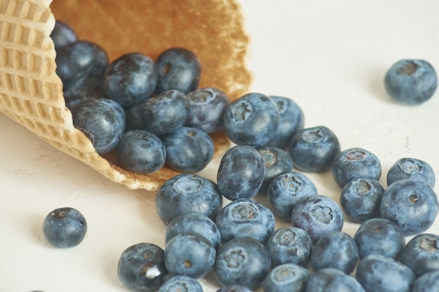 Close up of waffle cone with blueberries on white concrete