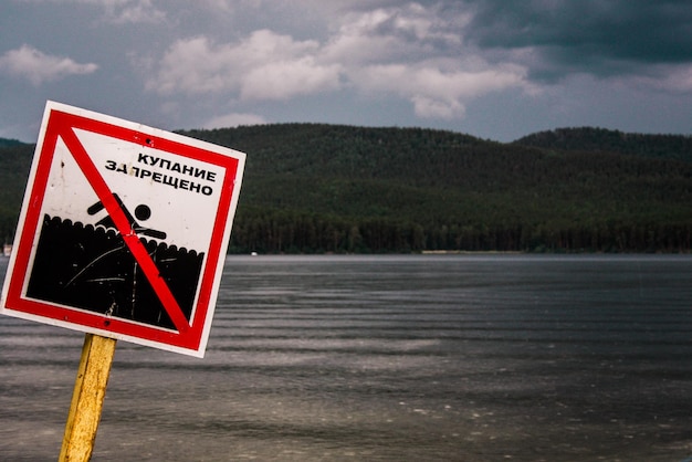 Photo close-up of warning sign by lake against sky