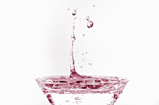 Close-up of water drop falling into a glass on white background.