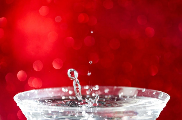 Close-up of water drop falling into a glass on white background.