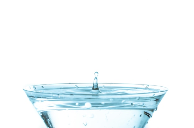 Close-up of water drop falling into a glass on white background.