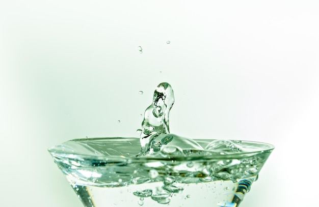 Close-up of water drop falling into a glass on white background.