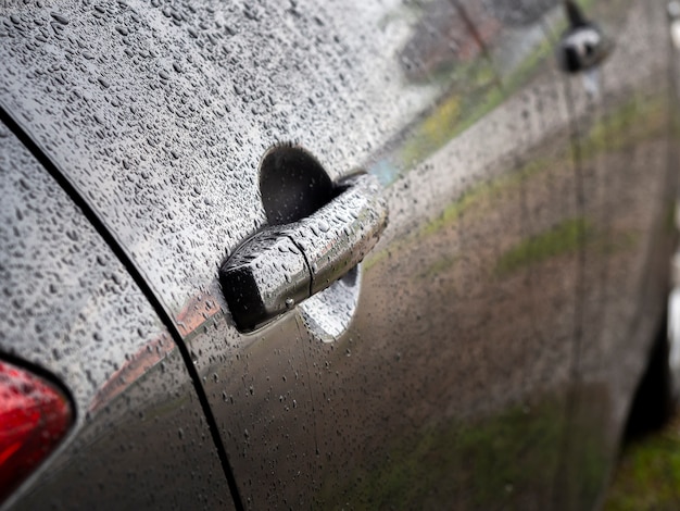 Close up of water drops on dark gray car after rain.