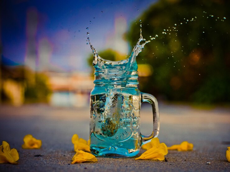 Photo close-up of water splashing in jar amidst flowers on road