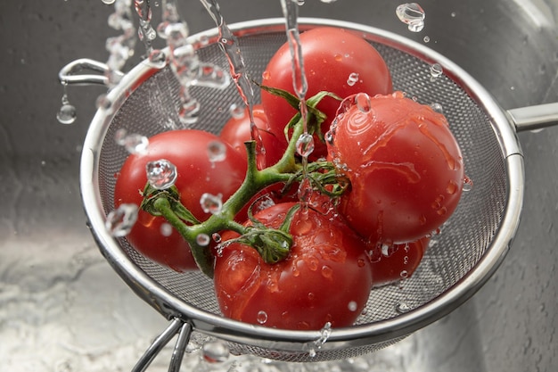 Photo close-up of water splashing on tomatoes in colander at sink