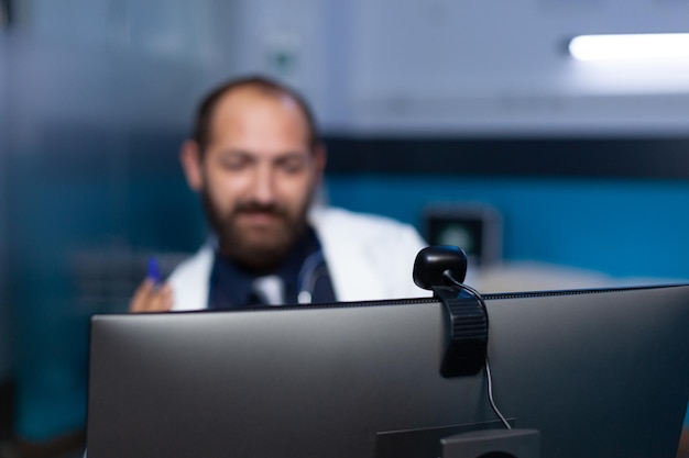 Close up of webcam on computer for video call used by doctor\
for remote consultation with patient. medic talking on online\
conference for checkup appointment, working late at night.