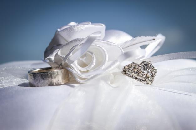 Photo close-up of wedding rings by artificial rose on pillow