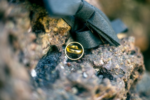 Photo close-up of wedding rings and tied bow on rock