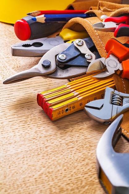 Close-up weergave hamer meetlint moersleutel tangen tang snijder potlood in gereedschapsriem op houten plank