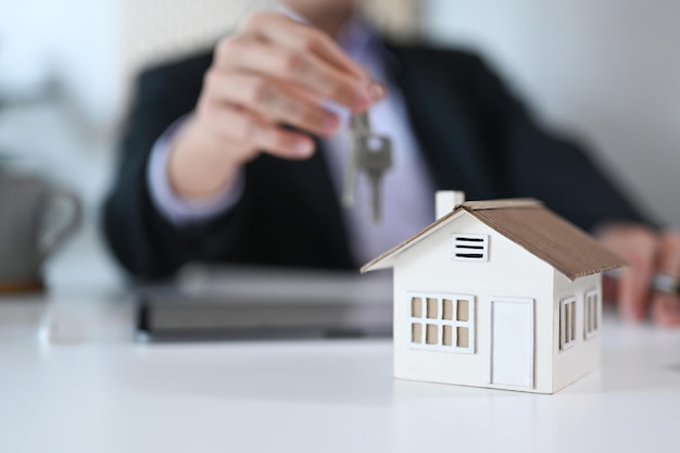 Close-up weergave huismodel op witte tafel en zakenman met sleutels op de achtergrond Onroerend goed verhuizen of onroerend goed huren