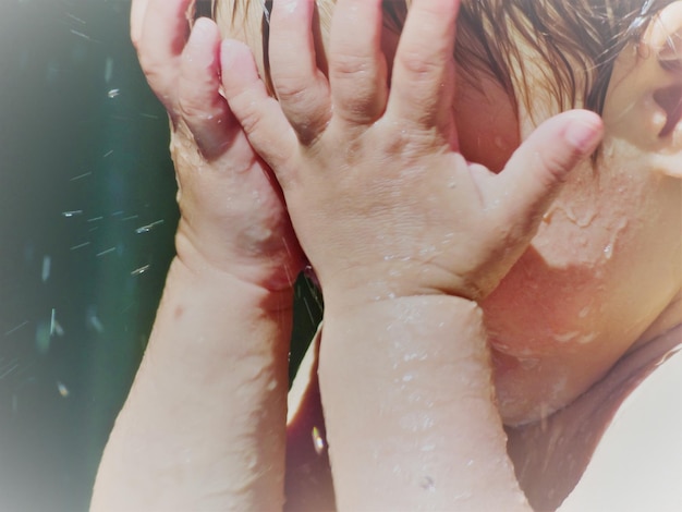 Close-up of wet boy covering face while standing outdoors