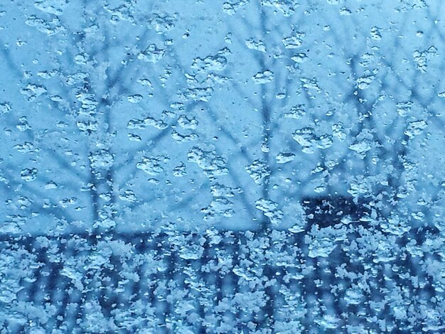 Close-up of wet glass window against blue sky