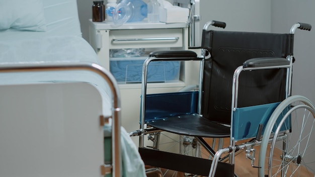 Close up of wheelchair in hospital ward for healthcare\
diagnosis and treatment. nobody in bed at intensive care with\
oxygen tube and heart rate monitor for assistance and\
recovery.