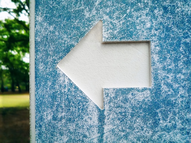 Foto simbolo bianco della freccia del primo piano sul vecchio segnale stradale ciano