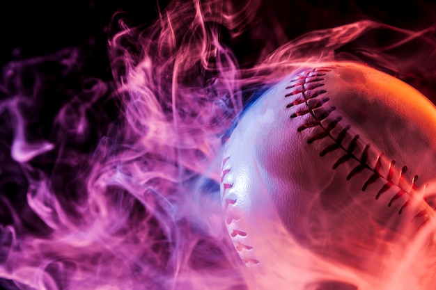 Photo close up of a white baseball ball in multi-colored red smoke from a vape on a black isolated background