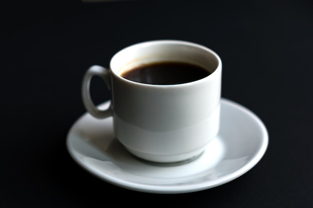 Close up of white cup of coffee on black background. Soft focus