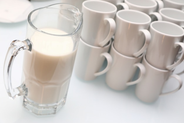 Close-up of White cups and a jug of milk on a light table