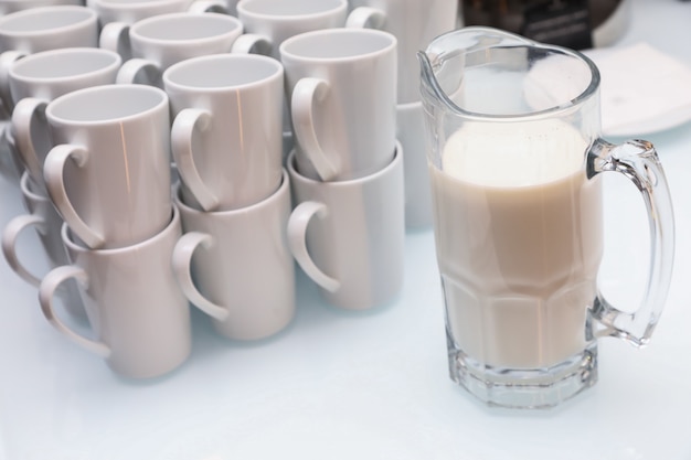 Close-up of White cups and a jug of milk on a light table