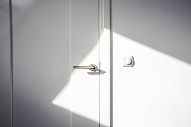 日光と白いドアをクローズアップ。クロムドア、空およびきれいな壁の現代設計のライトスイッチ