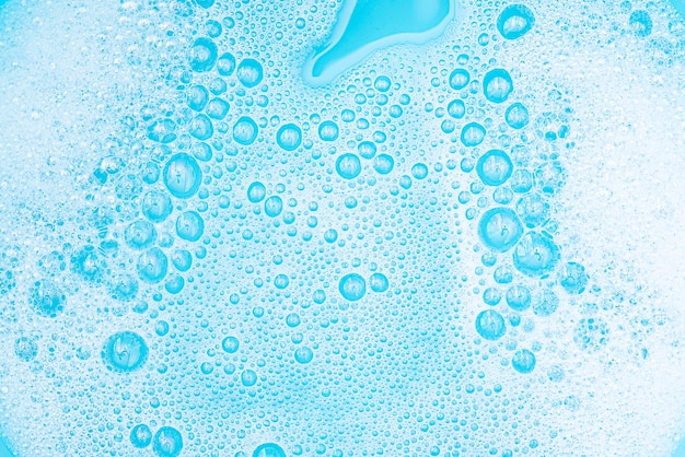 Photo close-up white foam with bubbles on surface of water, washing powder with soap and blue bath, abstract background transparent bubble.