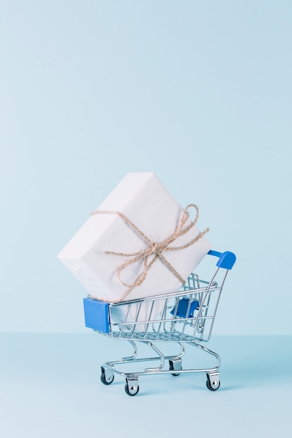 Close-up of white gift box in shopping cart on blue background