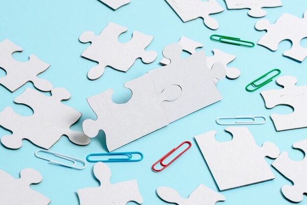 Close-Up White Jigsaw Pattern Puzzle Pieces To Be Connected With Missing Last Piece Positioned On A Flat Lay Background With Different Texture And Paper Supplies Accesories