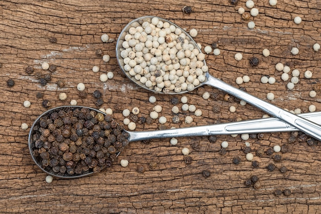 Close up of white peppers and black peppers on a spoon on wooden table