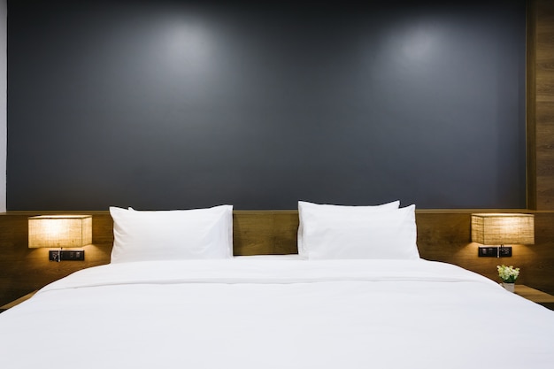 Close-up of white pillow on bed decoration with light lamp in hotel bedroom interior.