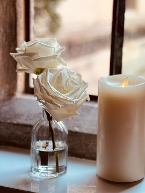 Foto close-up di una rosa bianca con un vaso di vetro sul davanzale della finestra
