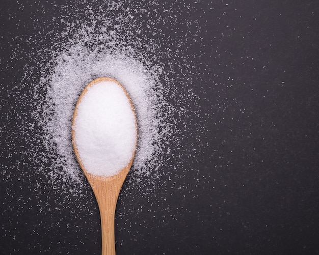 Photo close up white salt in wooden spoon and doctor stethoscope on black stone table