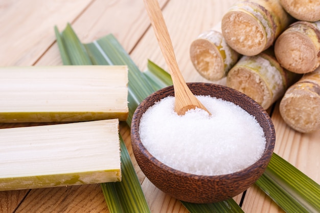 Close up white sugar and sugar cane on wooden table background
