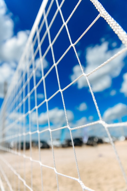 Close up of white volleyball net with blur background of blue sky and sandy beach. Place for outdoors activity near water.