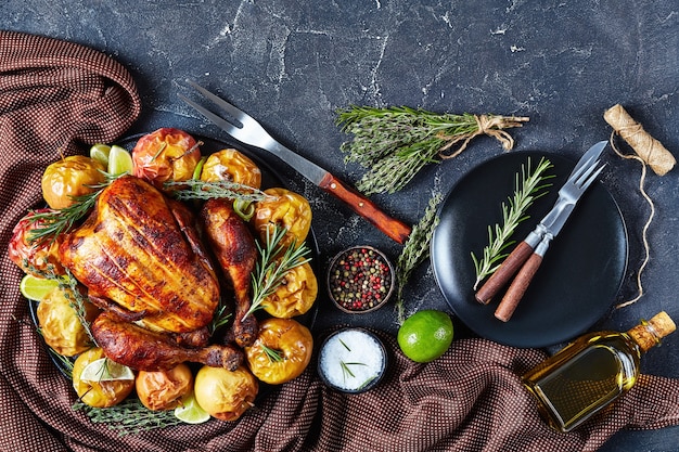 Close-up di un intero girarrosto di pollo servito su un piatto nero con mele cotte ed erbe aromatiche su un tavolo di cemento