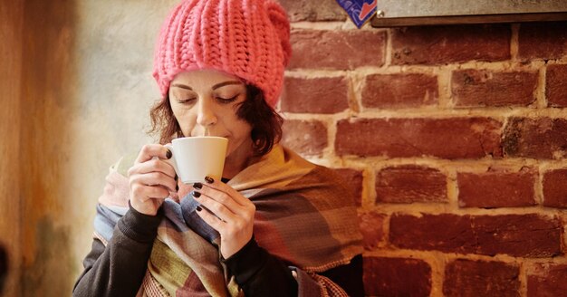 Close up winter portrait of a happy and beautiful young lady in a pink knitted beanie hat. She drink coffee