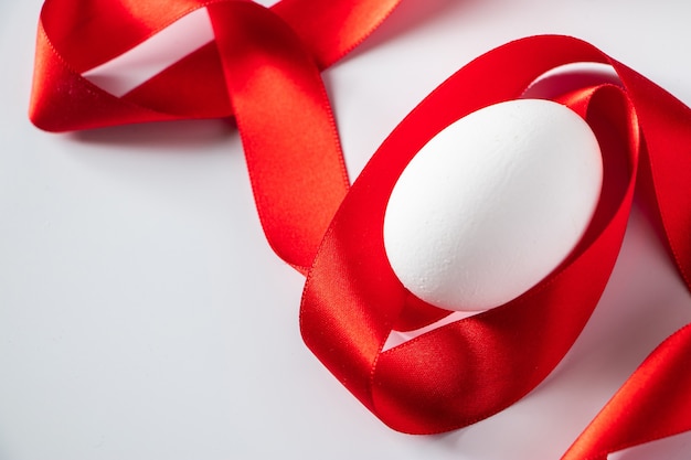 Close-up wit ei met rood zijdelint, Pasen-symbool op een lichte achtergrond